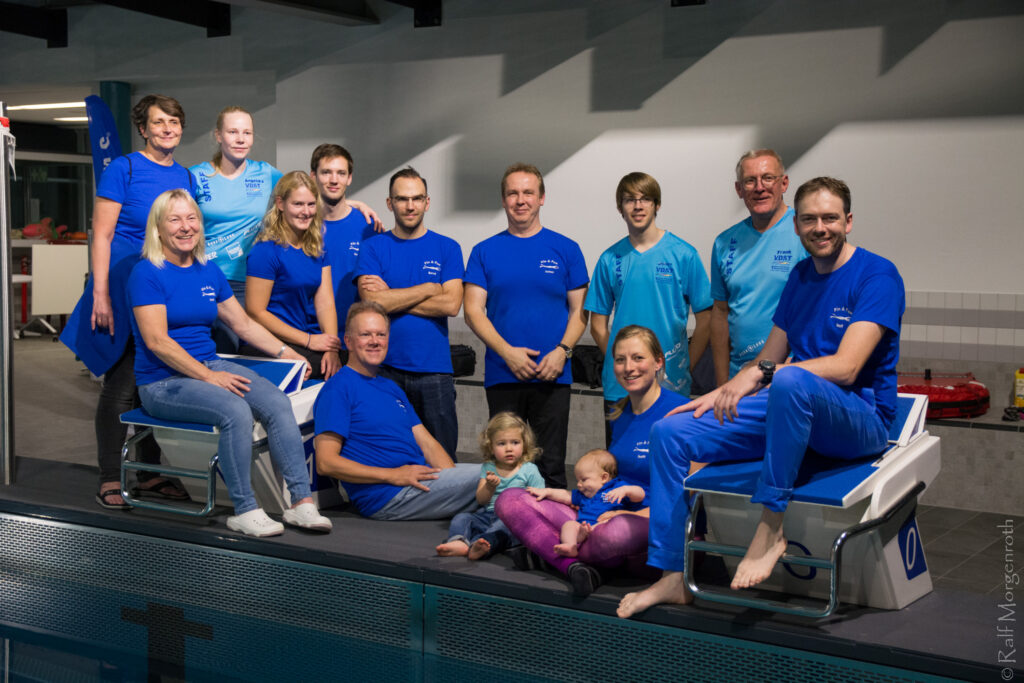 Mitglieder des Vereins sitzen für ein gemeinsames Foto auf den Startblöcken eines Schwimmbads